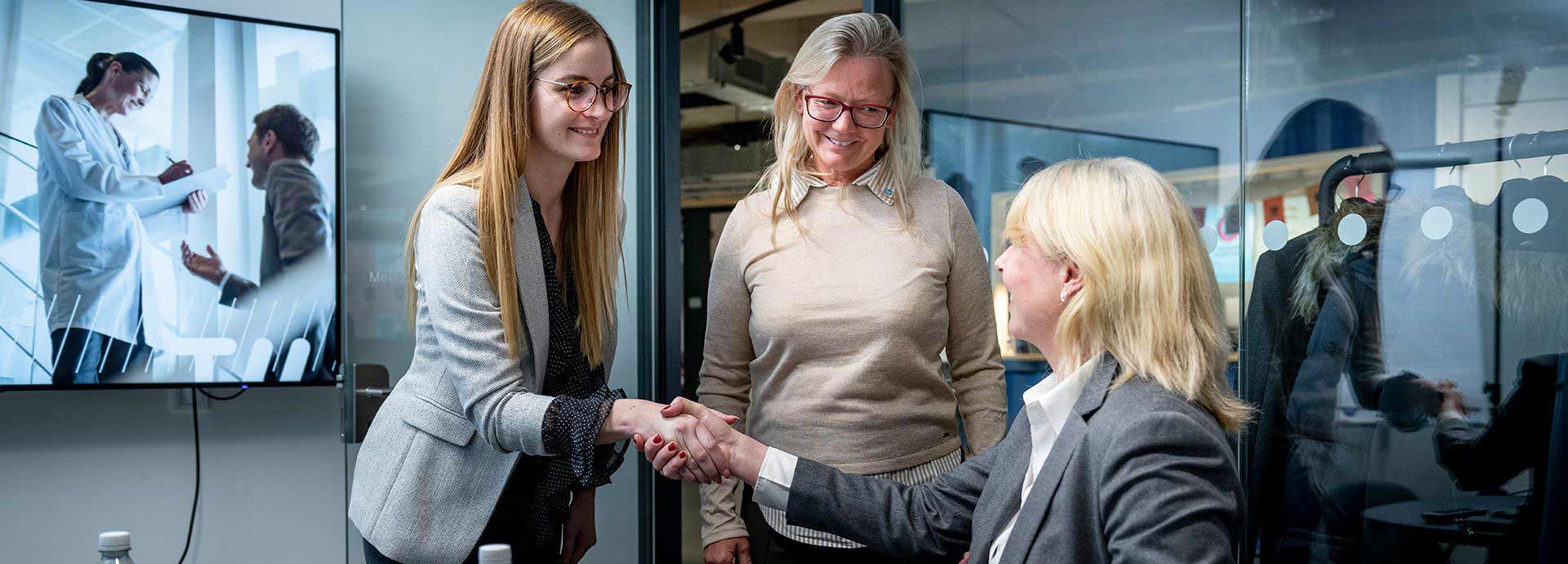 Three employees, two of whom shake hands