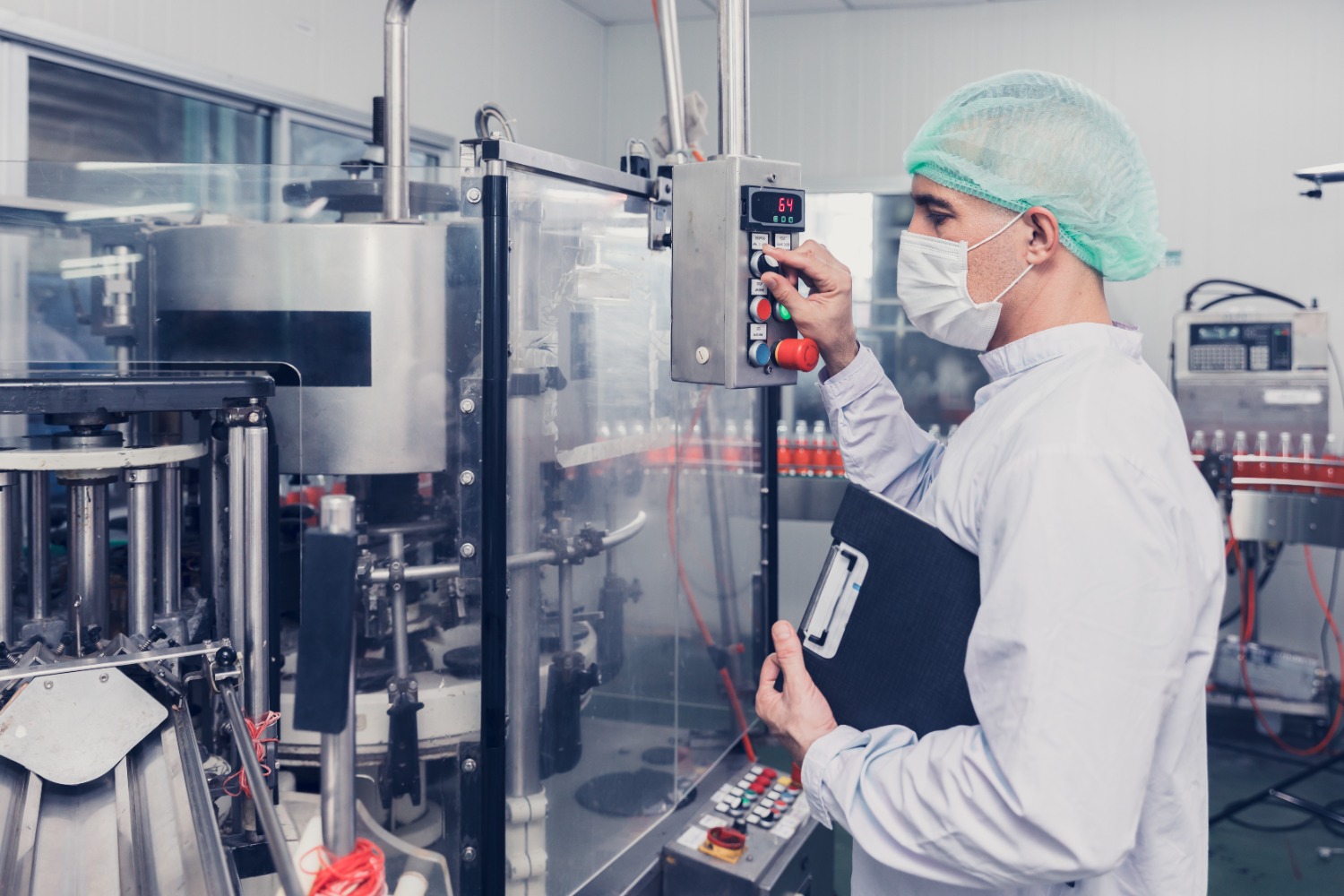 Operator in een hygiënische productieruimte, bedient een machine en bewaakt het productieproces met een clipboard in de hand