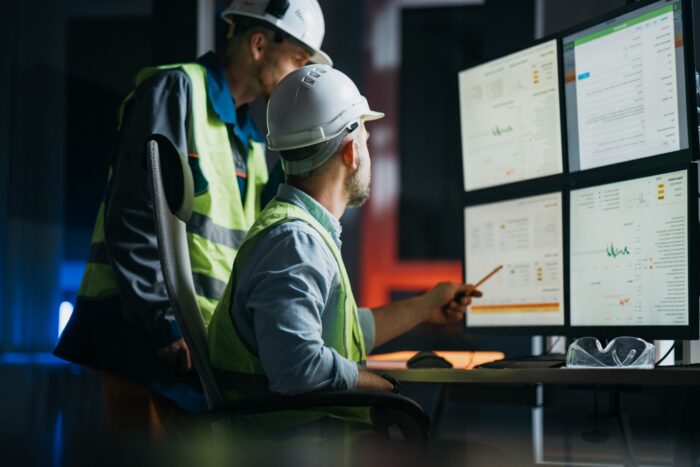 Operators in veiligheidsvesten en helmen analyseren op meerdere computerschermen in een controlekamer