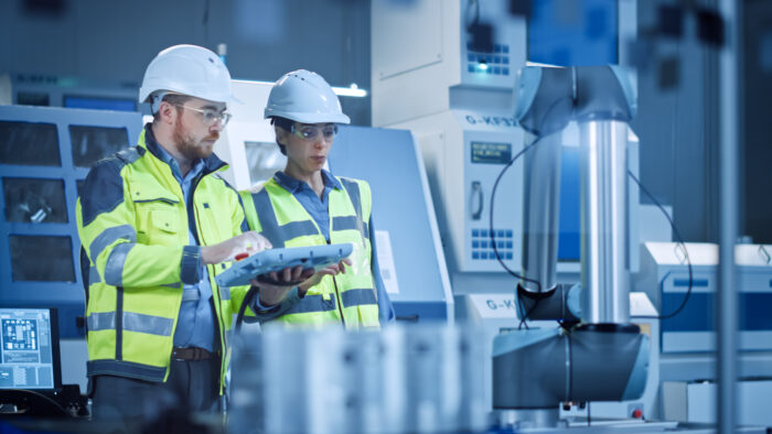 Twee operators met veilgheidshelmen en jassen bedienen een machine in een fabriek
